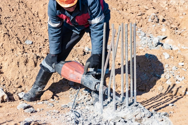 A worker with a jackhammer breaks concrete piles felling the\
pile head with a hand tool preparation of piles for mounting the\
foundation