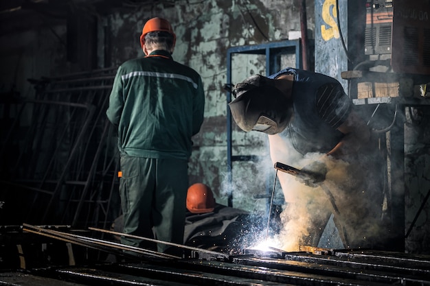 A worker with a protective mask is welding metal using a welding machine