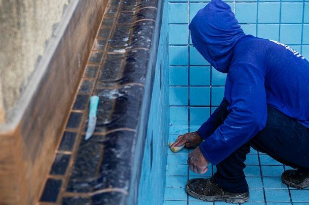 Worker with sponge cleaning pool to apply grout between tiles