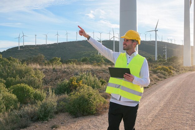 Worker with a tablet points and looks toward renewable energy windmills