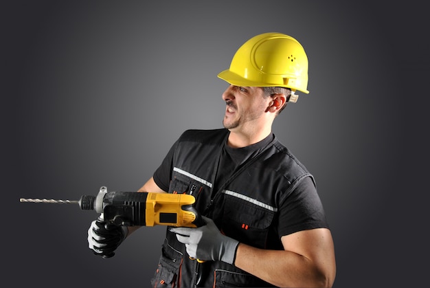 Worker with yellow helmet, drill and hammer