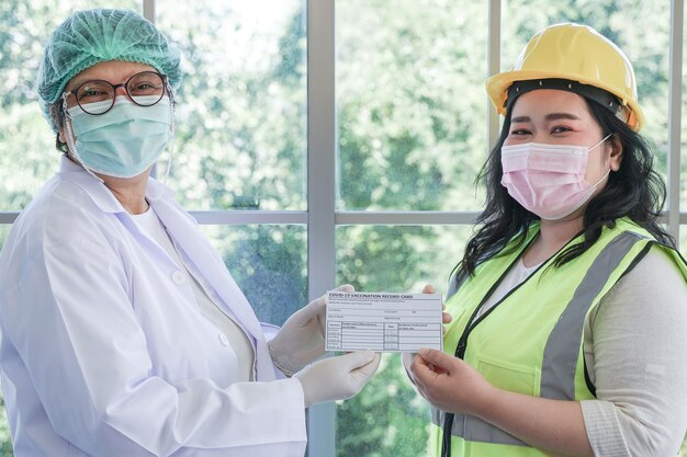 Worker woman and nurse showing Covid 19 vaccination record card after injecting vaccine