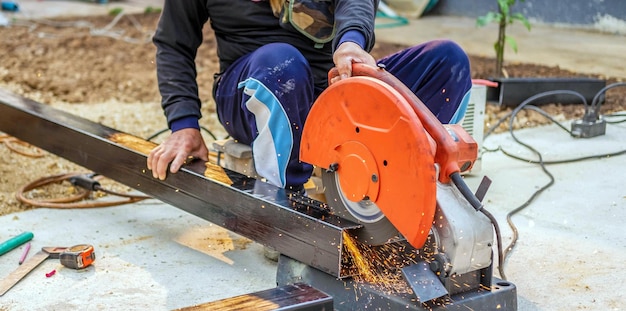 Photo worker in the work clothes uses an electric steel cutter cutting large steel bars