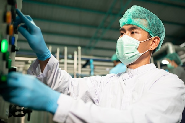 Worker working in drink factory at conveyor belt with fruit juice glass bottled in production line