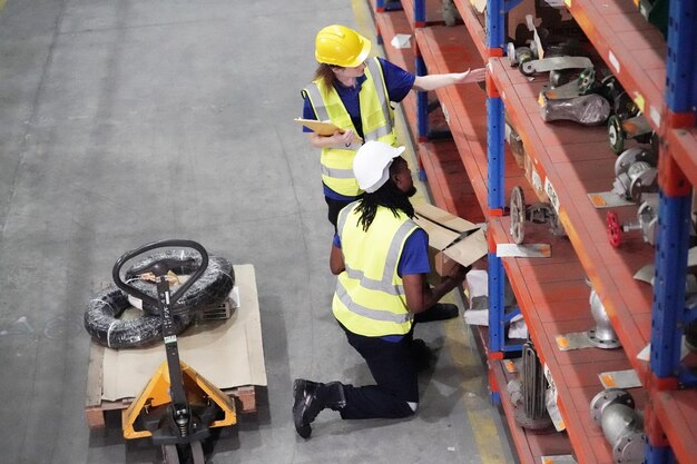 L'operaio che lavora in un grande magazzino tiene l'elenco di controllo delle tabelle cartacee controllando il materiale confrontato con le scatole avvolte in plastica conservate su pallet di legno pronte per la spedizione al cliente