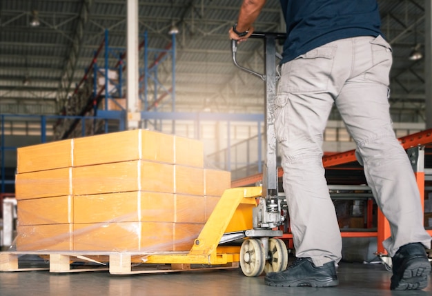 Worker working with hand pallet truck unloading cargo boxes at the warehouse.