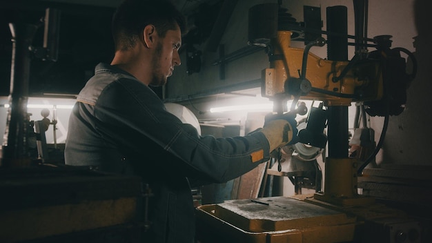 A worker works on a metal drilling machine in a workshop