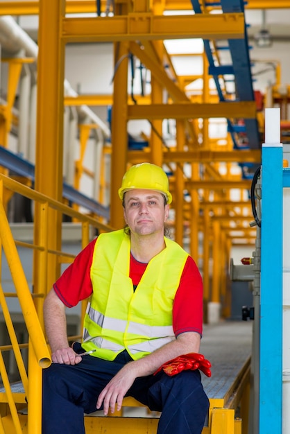 Photo worker in yellow reflective suit with yellow helmet sitting in a factory