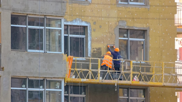労働者は、エレベーター パンの作業員と建物の建設現場の壁を断熱しています。