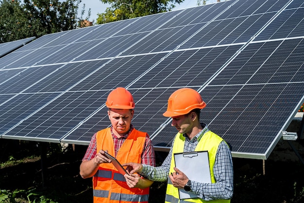 Workers checking work of solar panel station and discussing it tablet