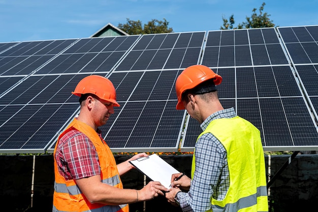 Workers checking work of solar panel station and discussing it with tablet