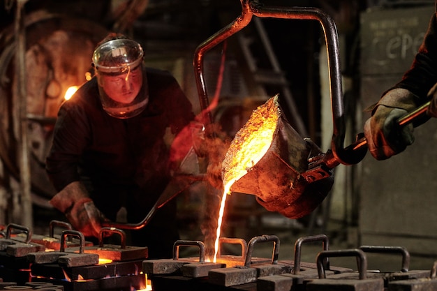 Workers in helmets working in team they melting iron in metal factory