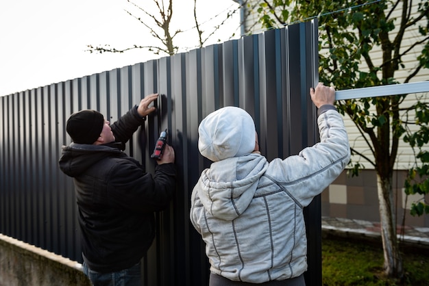 Workers install of gray fence from metal profile