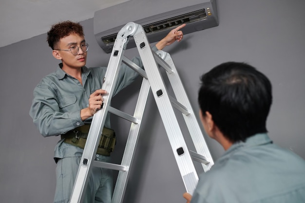 Workers installing air conditioner on wall in house of client