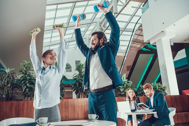 Photo workers making exercises with dumbbells in office.