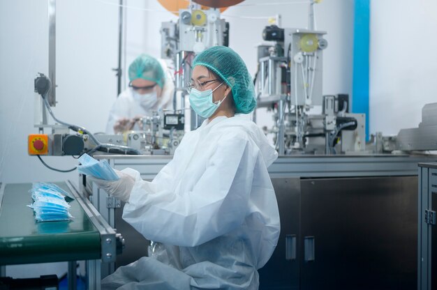 Workers producing surgical mask in modern factory, Covid-19 protection and medical concept.