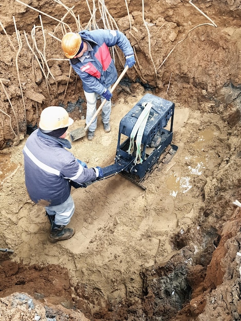 Foto i lavoratori tamponano il terreno con uno speciale strumento di lavoro compattatore o piastra vibrante preparazione della fondazione