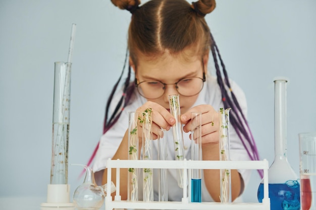 Photo workes with liquid that is in test tubes little girl in coat playing a scientist in lab by using equipment