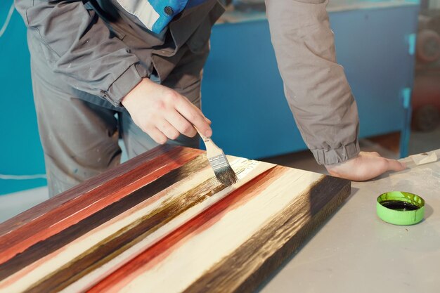 A working cabinetmaker holds a brush in his hand and paints a wooden surface A trace of paint on a wooden board