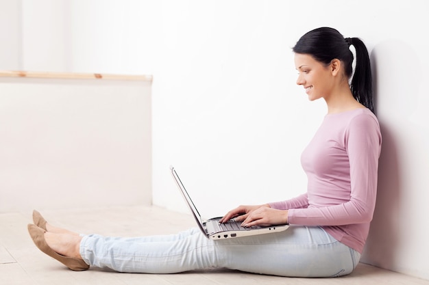 Working at the computer. Beautiful young woman sitting on the floor and using computer