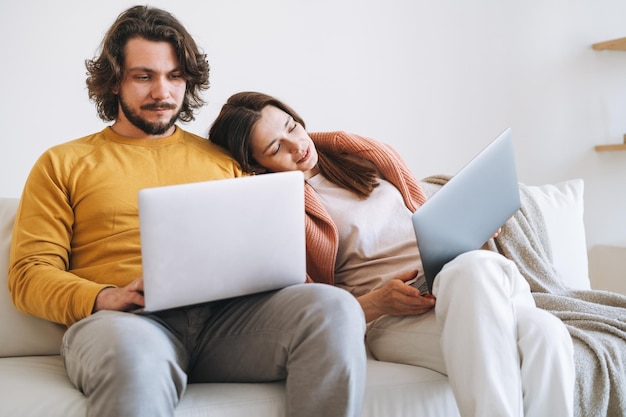 Working couple young family using laptop on sofa in living room\
at home