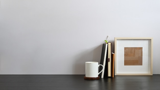 Working desk along with book, notebook, picture frame putting together on it with white cement wall . Orderly workspace concept.