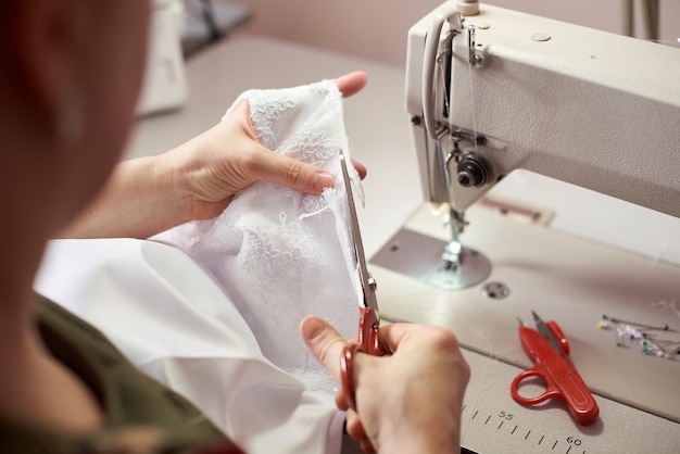 Mani femminili che lavorano usando le forbici per tagliare il tessuto durante il processo di cucitura vista ravvicinata sfondo sfocato