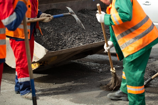 A working group of road workers loads the old asphalt into the bucket of the excavator