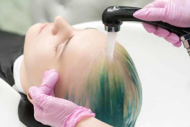 Working hairdresser in hair salon. Hairstylist hands wash hair with shampoo in shower in special sink