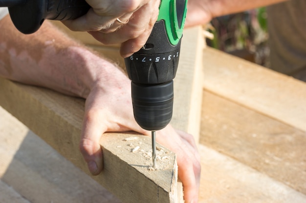 The working hands of a carpenter tightening an electric screwdriver screws into wood