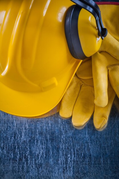 Working helmet safety earmuffs and yellow protective gloves on scratched metallic background construction concept