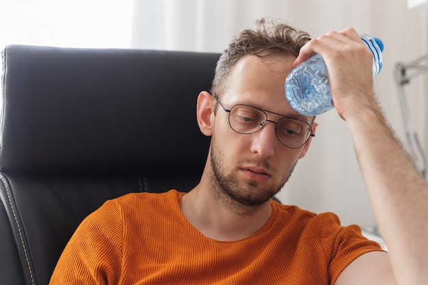 L'uomo che lavora a casa soffre di caldo e sete si raffredda con una bottiglia d'acqua nelle calde giornate estive