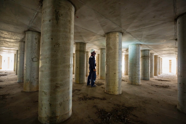 タンク設備トンネルの地下で働く男性の検査ポールタンクの下の内部の懐中電灯を使用することによって。