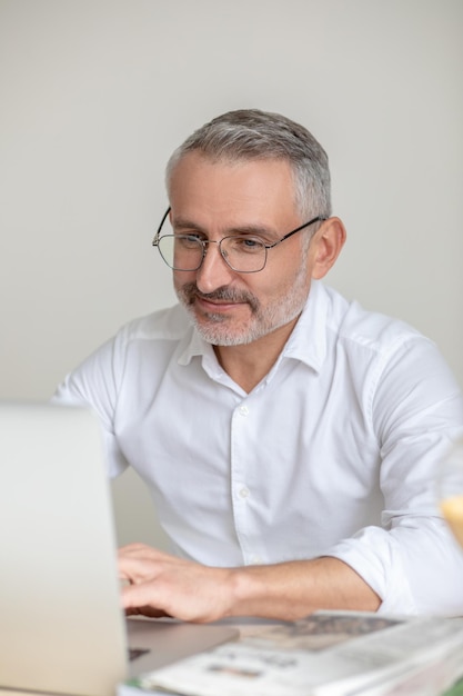 Working. A man in white shirt and eyewear working in the offcie and looking involved