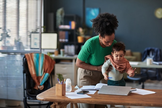 Working Mother Holding Child While Using Laptop at Home