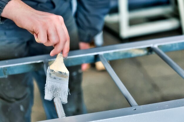 Photo working painter paints metal ladder with paint brush hand closeup with space for copying