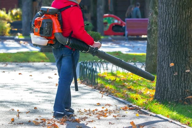 Photo working in the park removes leaves with a blower park cleaning service removing fallen leaves in autumn