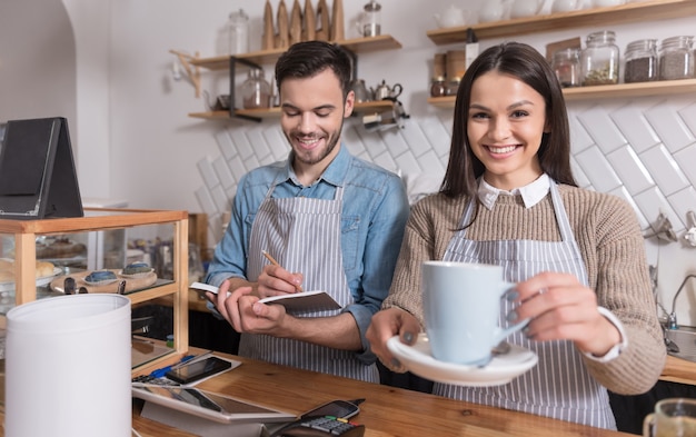 At the working place. Satisfied emotional waiters smiling and selling coffee while standing at the counter