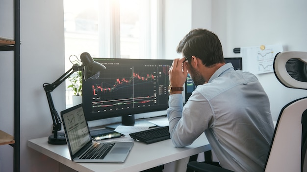 Premium Photo | Working process smart male trader looking at charts on multiple computer screens and analyzing data