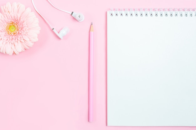 Working space: notepad, pencil, headphones and gerbera flower on pink background.