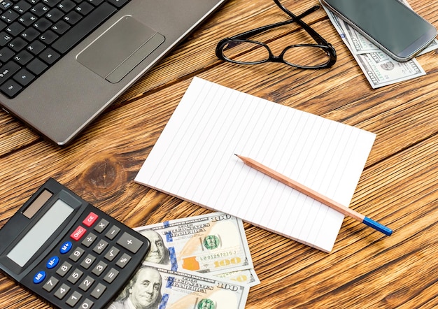 Working space with blank notepad laptop calculator glasses smartphone and money Business concept