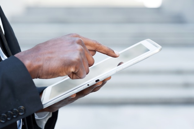 Lavorare su tablet. vista laterale immagine ritagliata di un uomo africano in abiti da cerimonia che lavora su un tablet digitale mentre si trova all'aperto