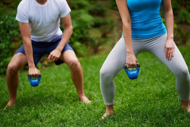 Foto lavorare quei muscoli ritagliata immagine di un uomo e di una donna che usano i pesi della campana del bollitore in una lezione di ginnastica all'aperto