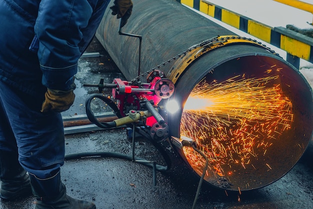 Il saldatore funzionante taglia il metallo e le scintille volano taglio a gas di tubi di grande diametro con acetilene e ossigeno taglio di metalli industriali nell'industria petrolifera e del gas