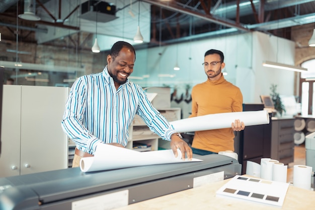 Working with colleague. Dark-skinned writer smiling while working with colleague in publishing office