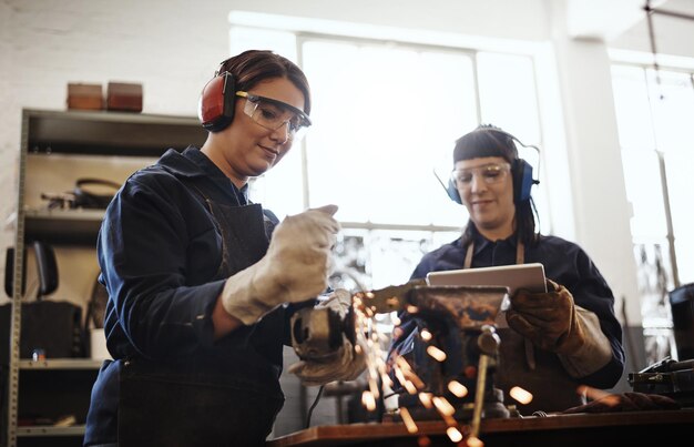 Photo working with metal cropped shot of two attractive young female artisans using an angle grinder in their workshop