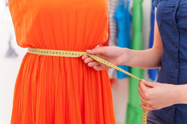 Working with new collection. Cropped image of woman measuring dress on the mannequin