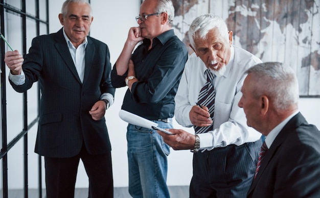 Lavorare con adesivi su vetro. il team di anziani architetti d'affari ha una riunione in ufficio.