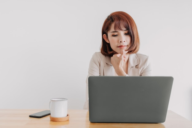 La donna lavoratrice sta usando il laptop sulla scrivania dell'ufficio con sfondo bianco