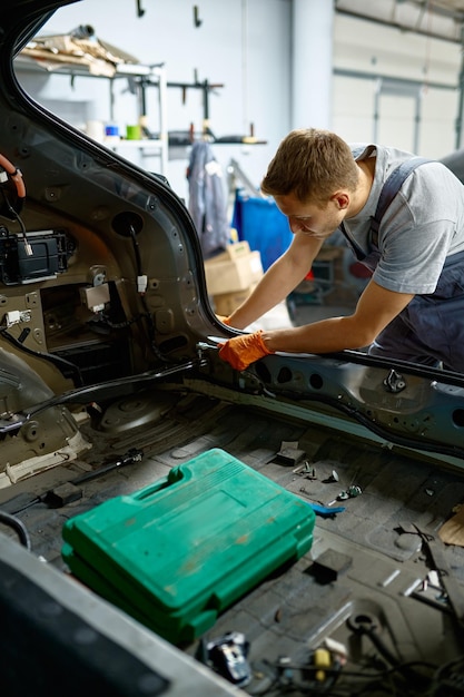 Workman fixing bolt during car body repair using special tools. Auto mechanic working in garage